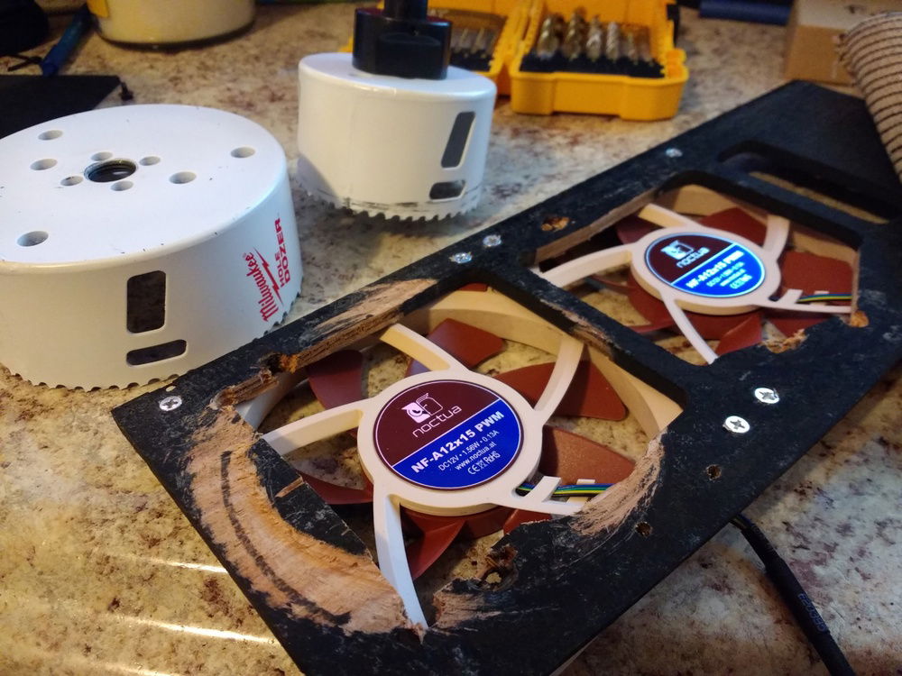 The two Noctua fans at the front of the case, behind the fabric, that drive most of the airflow. I widened the existing holes to let them breathe more, unsuccessfully with a hole saw (pictured), then with a jigsaw.