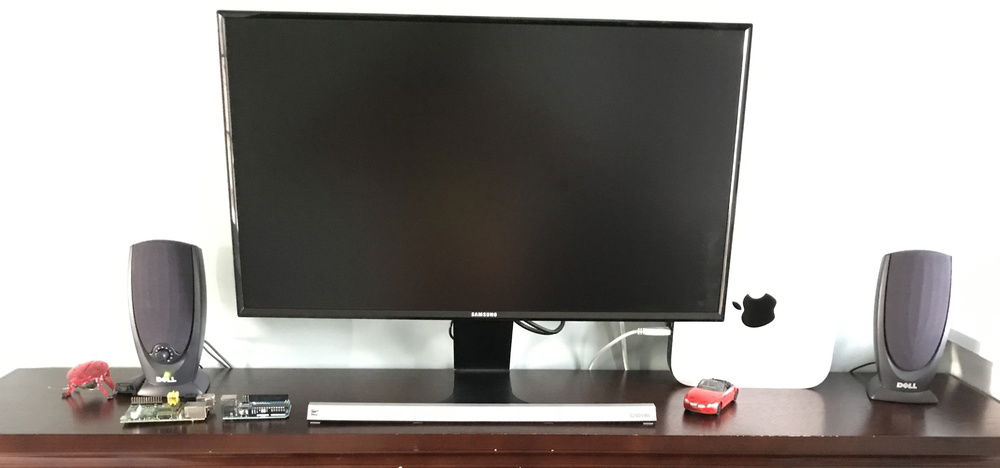 Monitor on the desk. Some old Dell speakers attached to the monitor and driven through HDMI audio. 2012 Mac Mini in background.